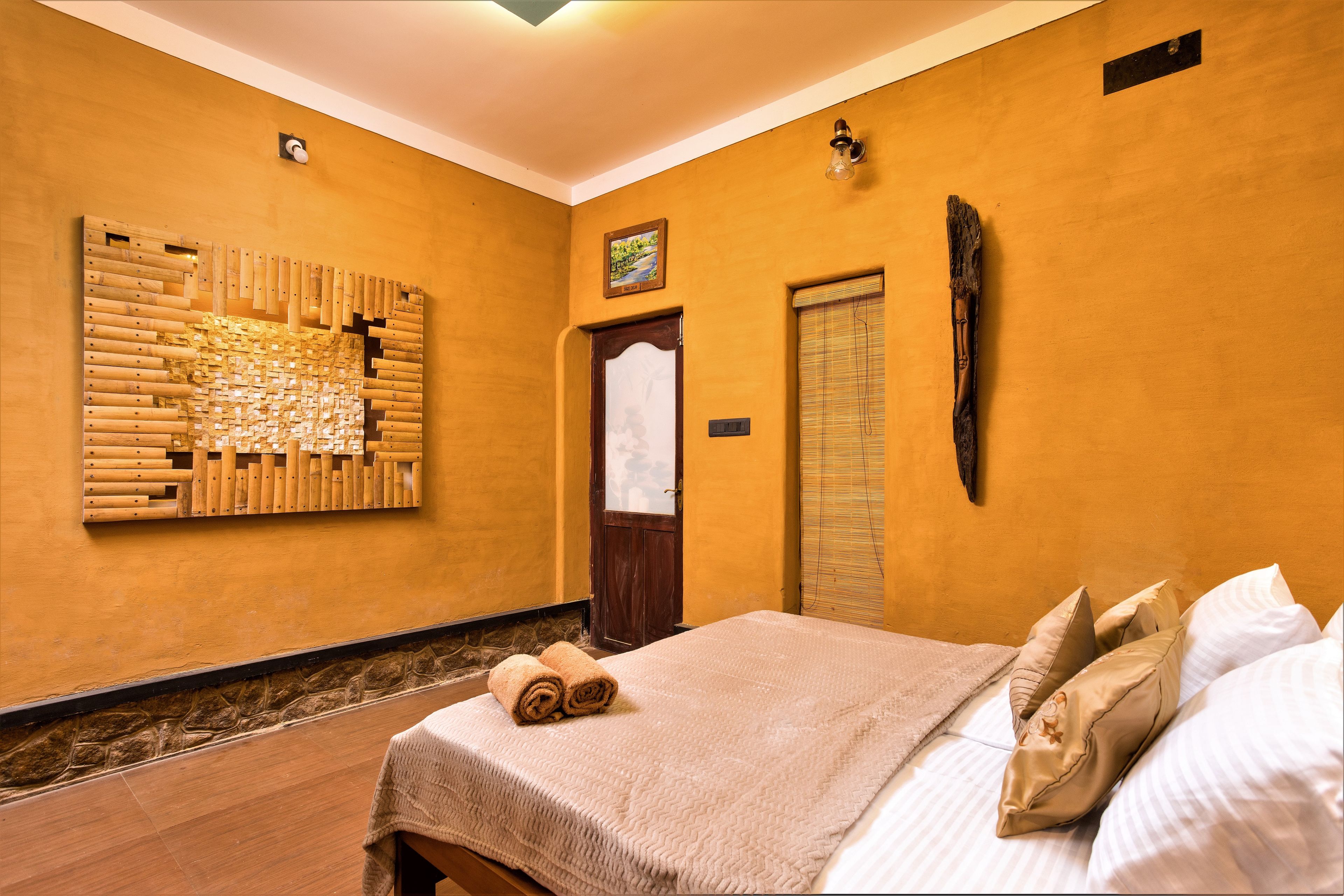 Quarto de hotel com cama, uma obra de arte na parede, porta e janela com persianas.