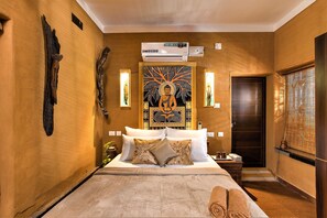 A hotel room with a large bed, a wall-mounted air conditioner, a decorative tapestry, and a wooden door.