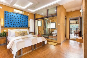 A modern hotel room with a large bed, a blue decorative wall, a glass shower enclosure, and a balcony with a view.