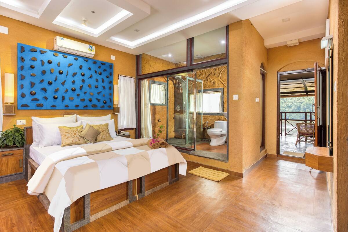 A modern hotel room with a large bed, a blue decorative wall, a glass shower enclosure, and a balcony with a view.