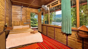 Una habitación de madera con una cama, un ventanal y un ventilador.