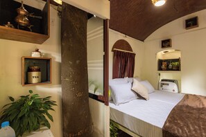 Una habitación con cama, estante con un recipiente para té, una planta y un espejo.