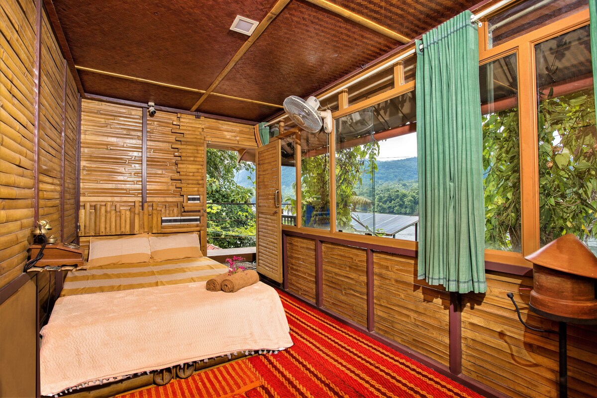 Una habitación de madera con una cama, un ventanal y un ventilador.