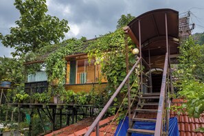 Una casa de madera con escalera y porche cubierto, rodeada de abundante vegetación.
