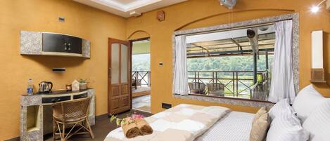 Habitación de hotel con cama, escritorio, silla, ventilador y ventana con vistas.