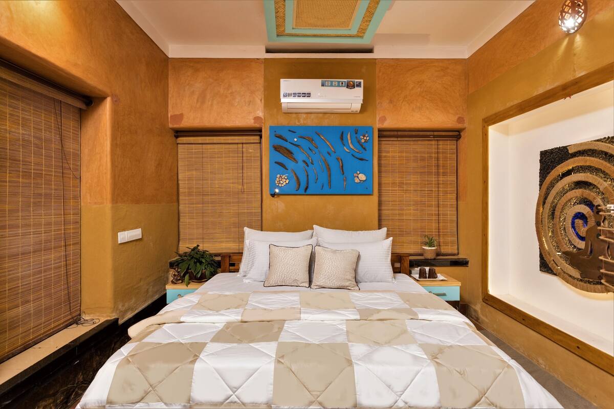 A bedroom with a bed, nightstands, a wall-mounted air conditioner, and a decorative wall piece.