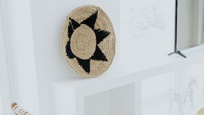 A room with two wooden chairs with woven seats, a round woven wall hanging, and a fireplace. - Pili Pala Suites (Paros)