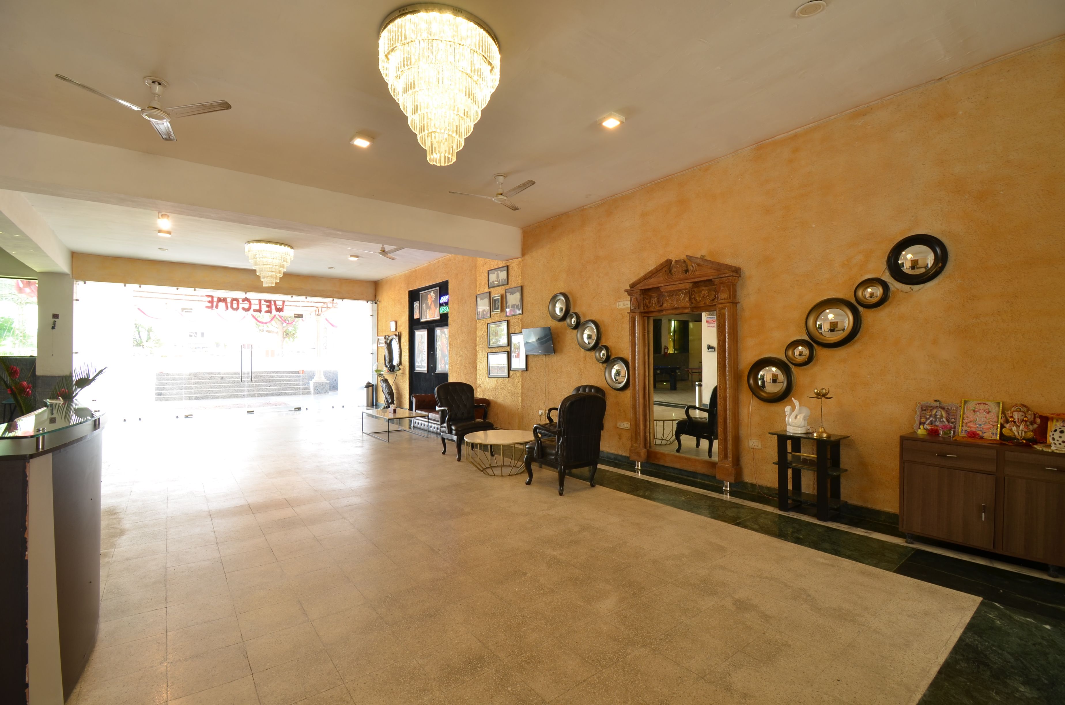 A hotel lobby with a reception desk, seating area, chandeliers, wall-mounted mirrors, and framed decorations.