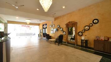 A hotel lobby with a reception desk, seating area, chandeliers, wall-mounted mirrors, and framed decorations.