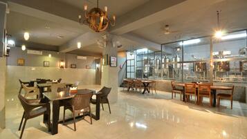A restaurant with multiple dining tables and chairs, a chandelier, ceiling fans, and large windows.