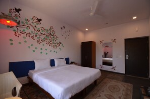 A bedroom with a bed, a chair, a wardrobe, a ceiling fan, and a wall decoration. - Hotel Royal Casa (Abu Road)