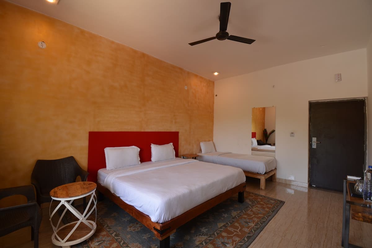Habitación de hotel con dos camas, un ventilador de techo, una mesita redonda y una puerta.