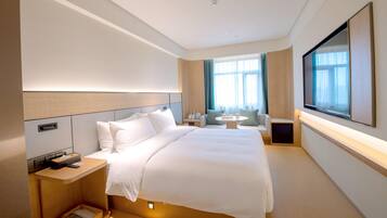 A modern hotel room with a large bed, bedside tables, a TV, and a window with curtains.