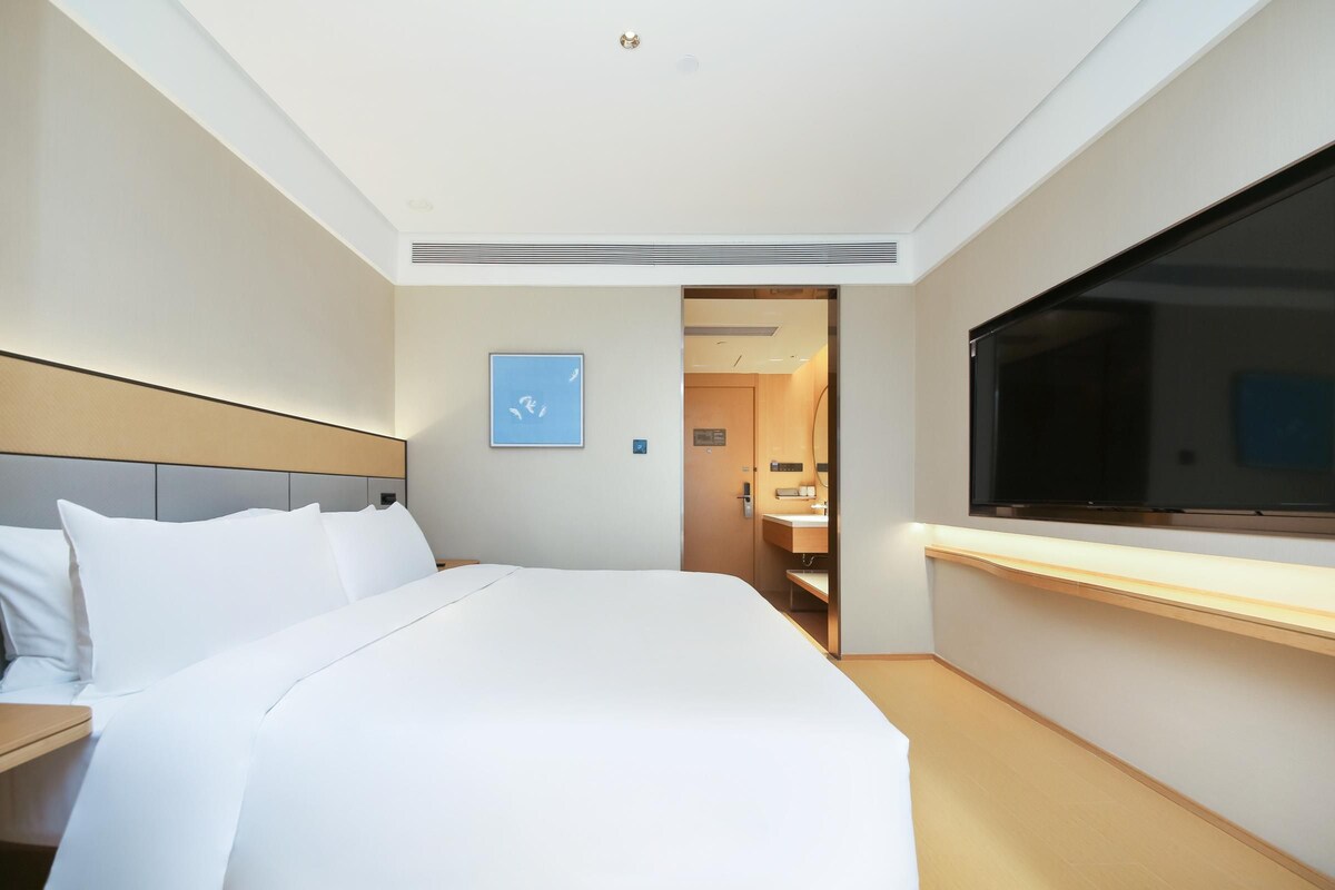 A hotel room with a bed, a TV, a bathroom, and a door leading to another room.