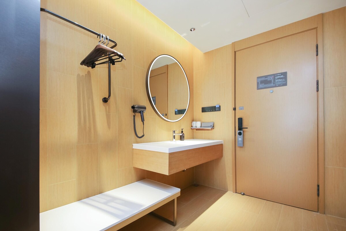 A modern bathroom with a wooden vanity, a bench, a mirror, a towel rack, and a door with a sign.