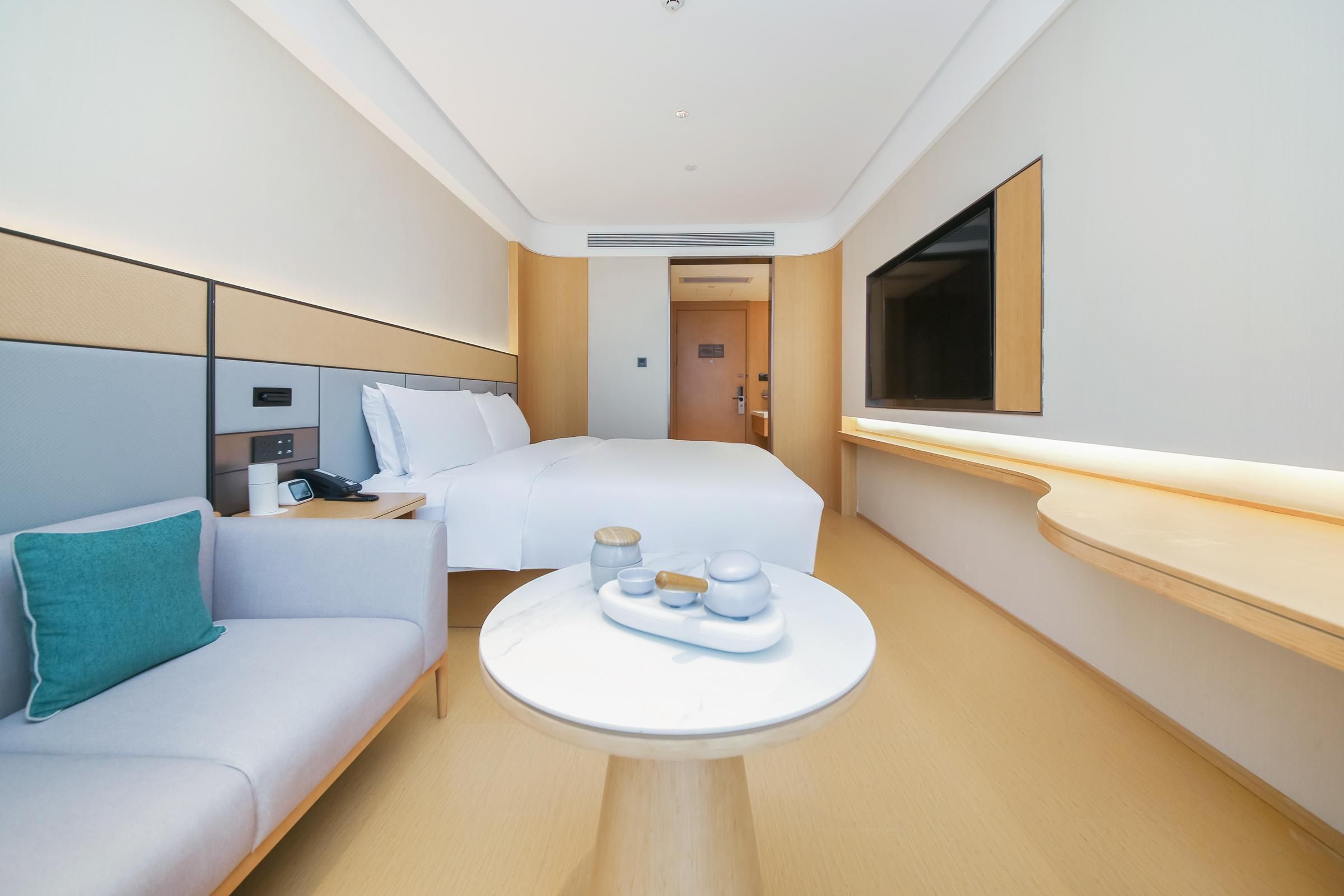 A hotel room with a bed, a sofa, a small table with a tray, a TV, and a door leading to another room.