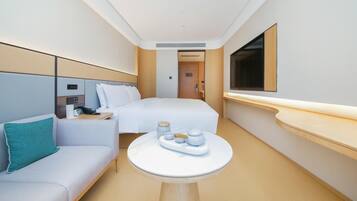 A hotel room with a bed, a sofa, a small table with a tray, a TV, and a door leading to another room.