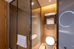 A modern bathroom with a glass-enclosed shower, a toilet, and a sink.