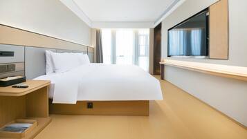 A hotel room with a bed, bedside table, TV, and a window with curtains.