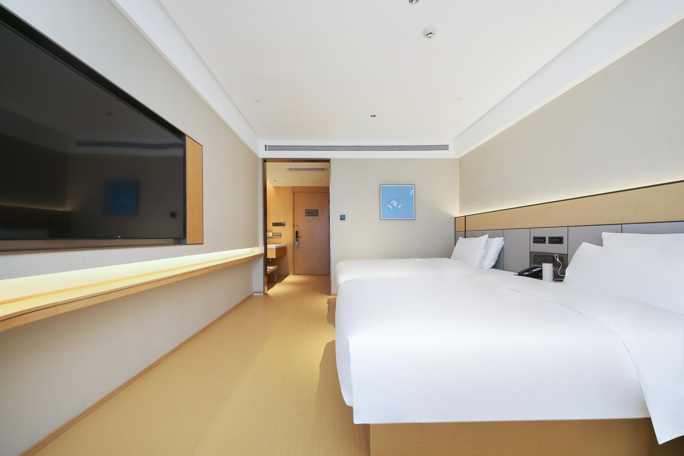 A hotel room with a large bed, a bedside table, a window, and a door leading to a hallway.