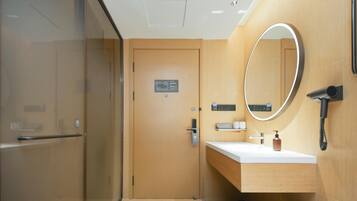Un baño moderno con cabina de ducha de vidrio, tocador de madera con espejo y perchero.