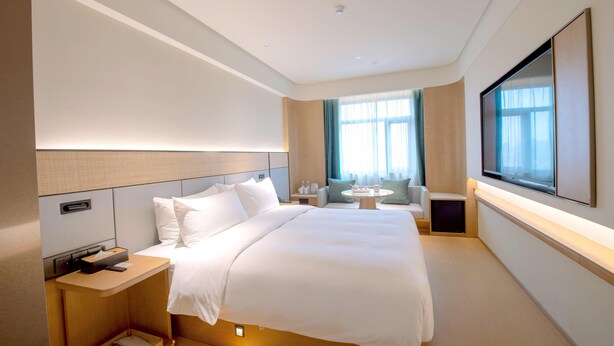 Ein modernes Hotelzimmer mit einem großen Bett, Nachttischen, einem Fernseher und einem mit Vorhängen versehenen Fenster.