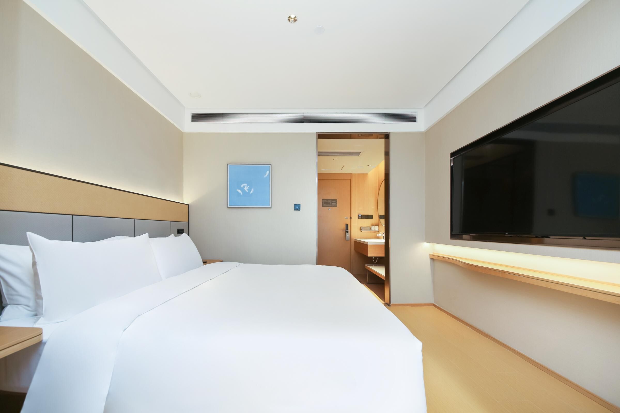 A hotel room with a bed, a TV, a bathroom, and a door leading to another room.