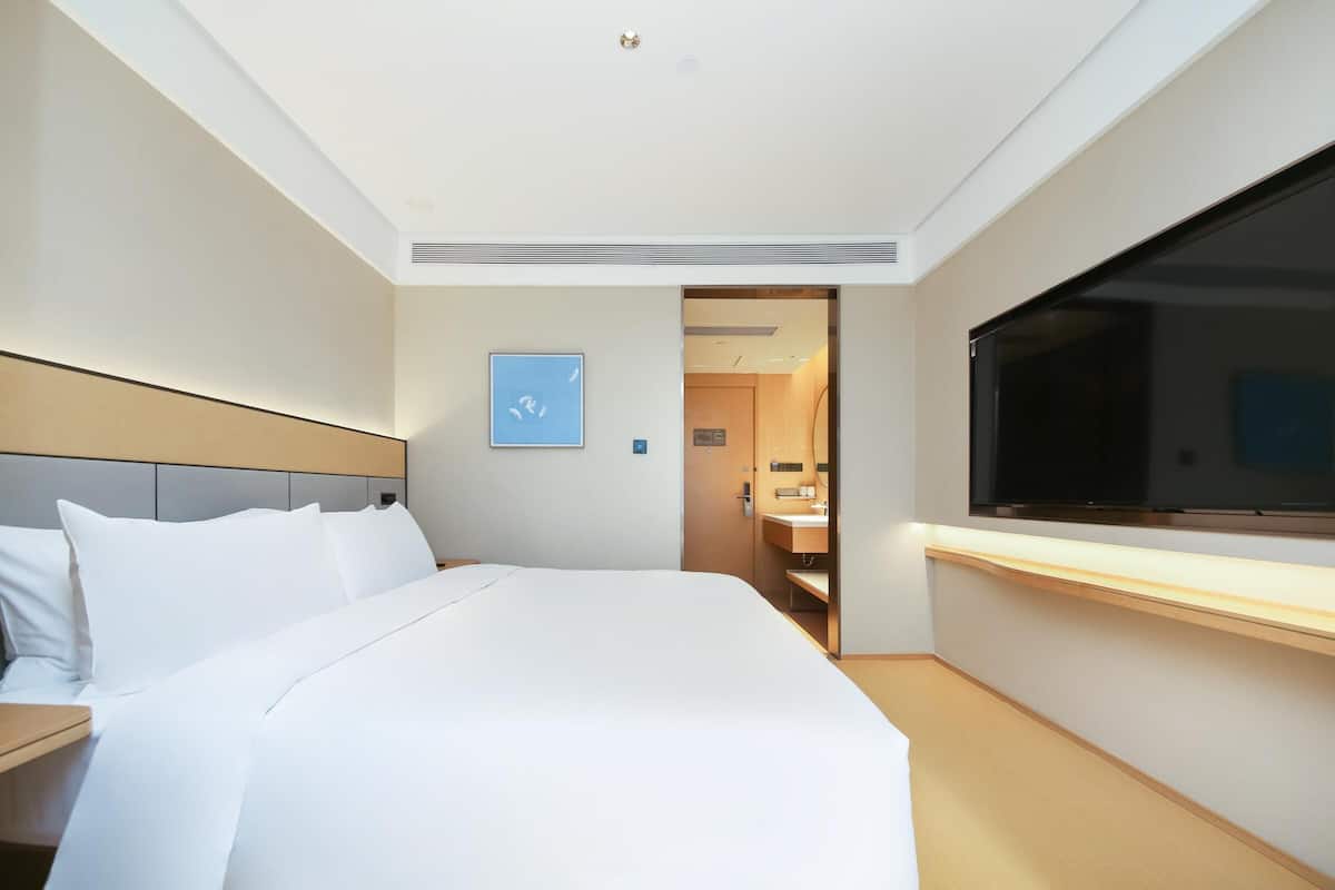 A hotel room with a bed, a TV, a bathroom, and a door leading to another room.