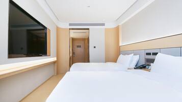 A modern hotel room with a large bed, a bedside table with a phone, and a TV mounted on the wall.