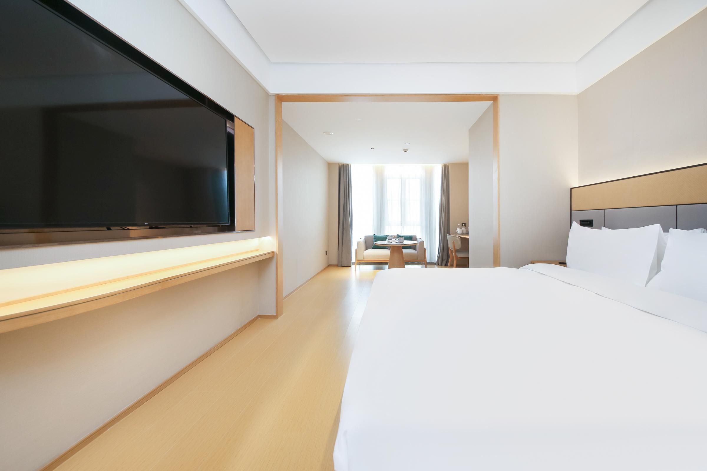 A hotel room with a large bed, a flat-screen TV, a desk, a chair, and a small table.