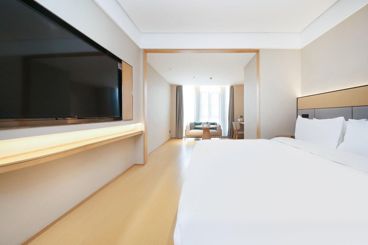 A hotel room with a large bed, a flat-screen TV, a desk, a chair, and a small table.