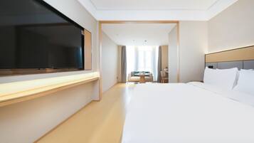 A hotel room with a large bed, a flat-screen TV, a desk, a chair, and a small table.