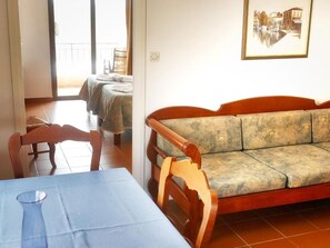 A room with a wooden sofa, a dining table with a vase, and a balcony with a view of buildings. - Areti Apart Hotel (Chania)