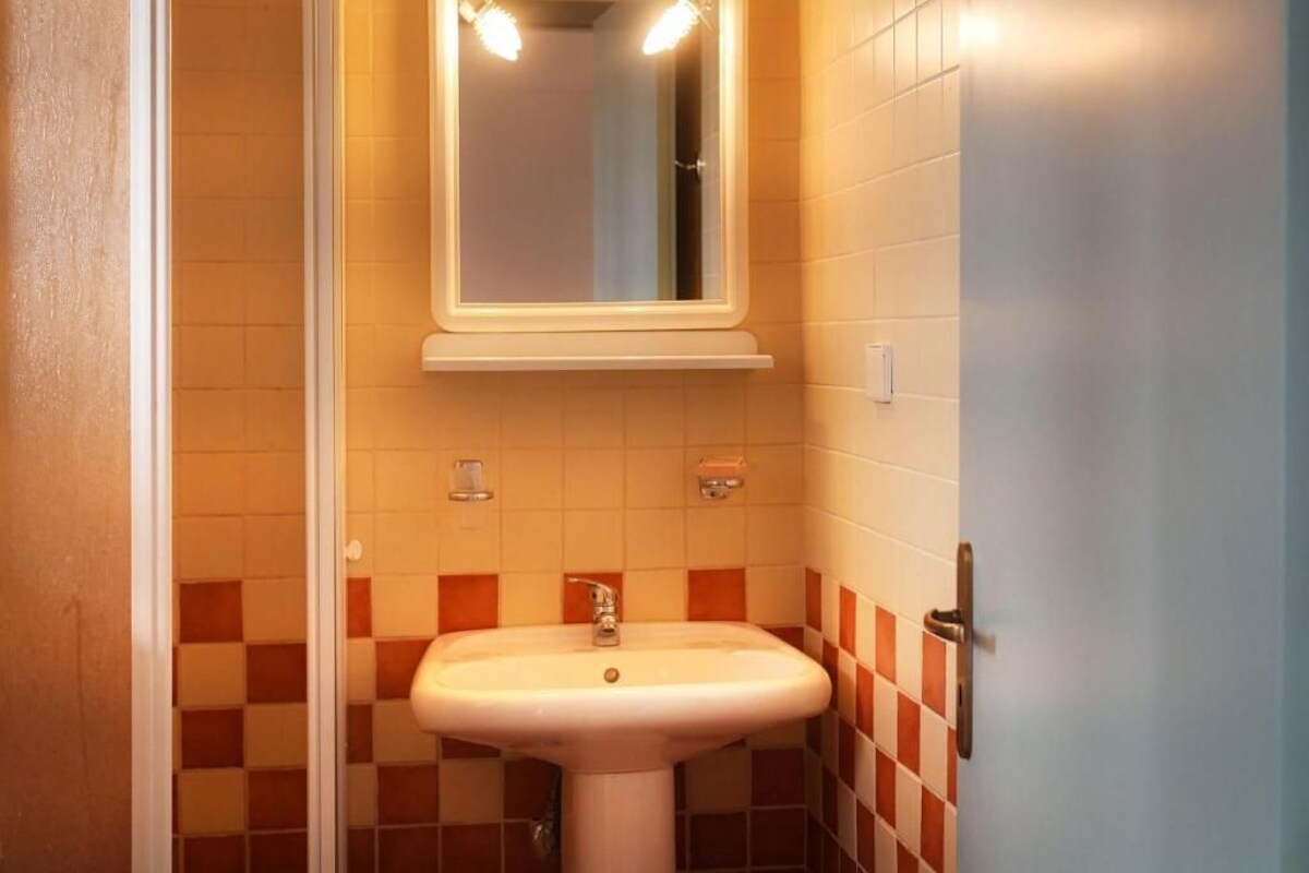 A bathroom with a white sink, a mirror with lights, and checkered tiles.
