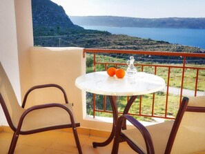 A balcony with a table, two chairs, a glass bottle, and two oranges. - Areti Apart Hotel (Chania)