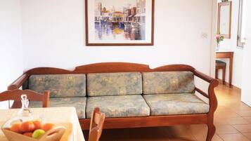 Una sala de estar con un sofá, una mesa con frutero y un cuadro enmarcado en la pared.