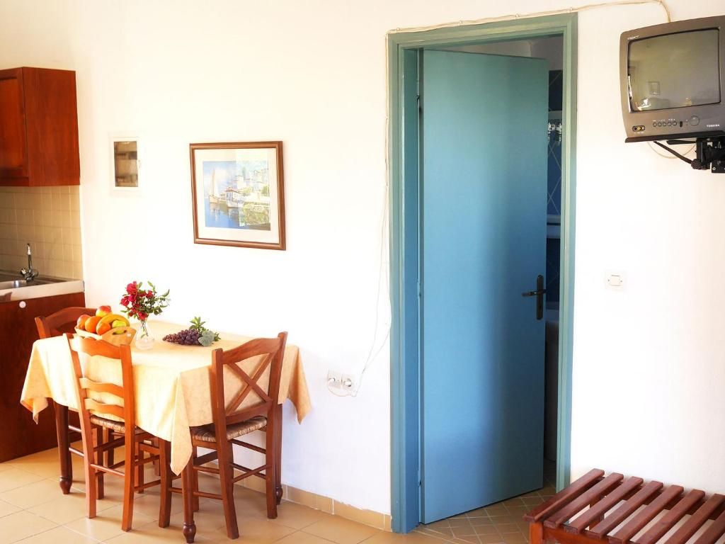 Un comedor con una mesa dispuesta para dos, una puerta azul y un televisor montado en la pared.