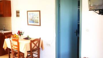 Un comedor con una mesa dispuesta para dos, una puerta azul y un televisor montado en la pared.
