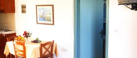 Un comedor con una mesa dispuesta para dos, una puerta azul y un televisor montado en la pared.