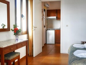 A room with a bed, a desk with a chair, a small kitchenette with a refrigerator and stove, and a window with curtains. - Areti Apart Hotel (Chania)