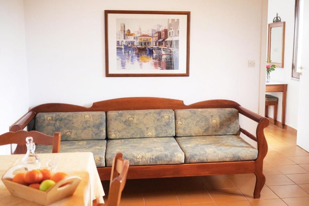 A living room with a sofa, a table with a fruit bowl, and a framed painting on the wall.