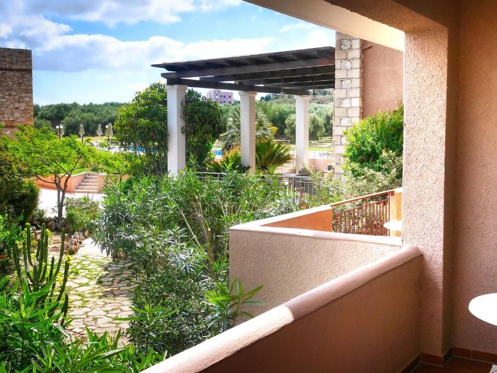 A balcony with a view of a garden, a pergola, and a pool area.