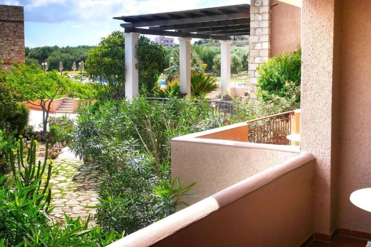 A balcony with a view of a garden, a pergola, and a pool area.