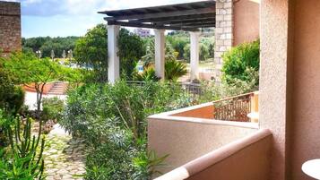 Un balcón con vista a un jardín, una pérgola y una zona de piscina.