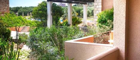 A balcony with a view of a garden, a pergola, and a pool area.