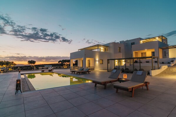 A modern house with a swimming pool, outdoor seating, and a view of the landscape. - Olive Garden Luxury Resort (Paros)
