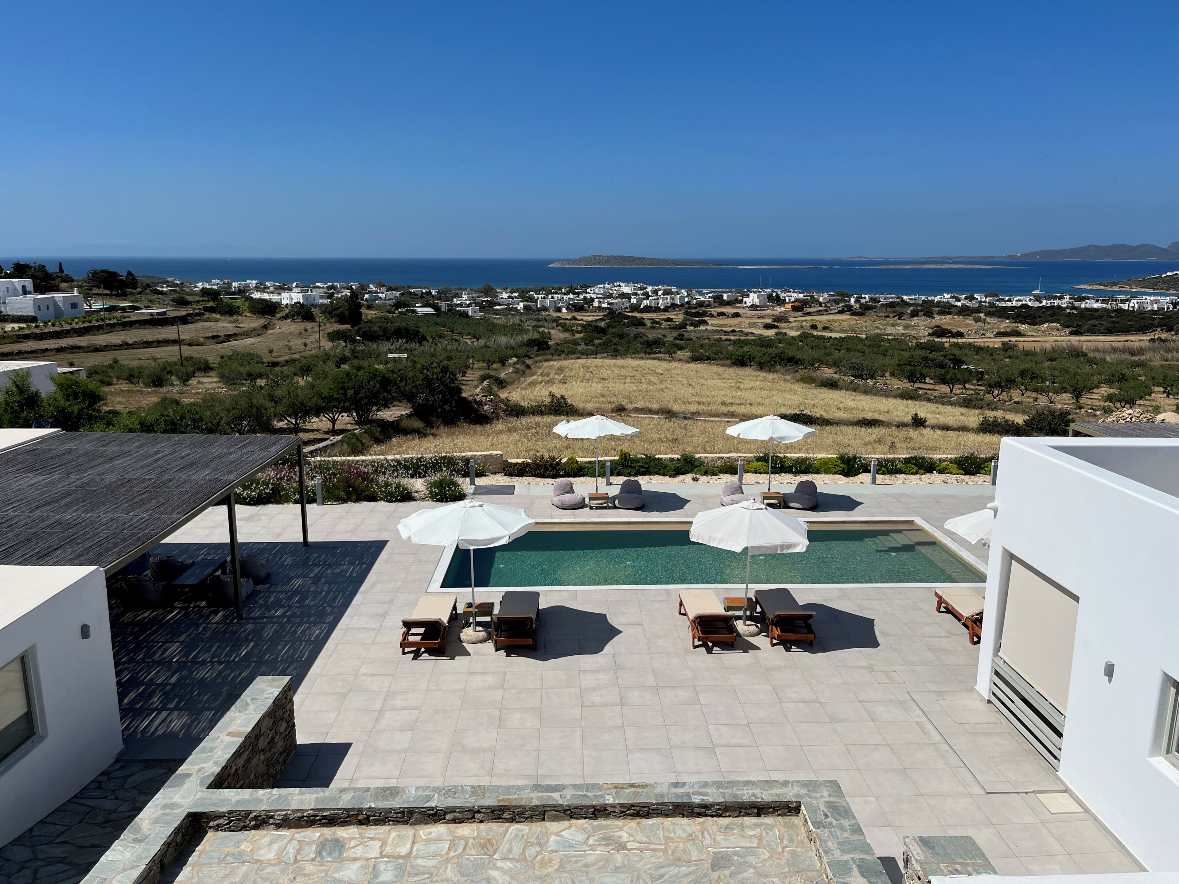 A rooftop pool area with lounge chairs and umbrellas, overlooking a coastal landscape.