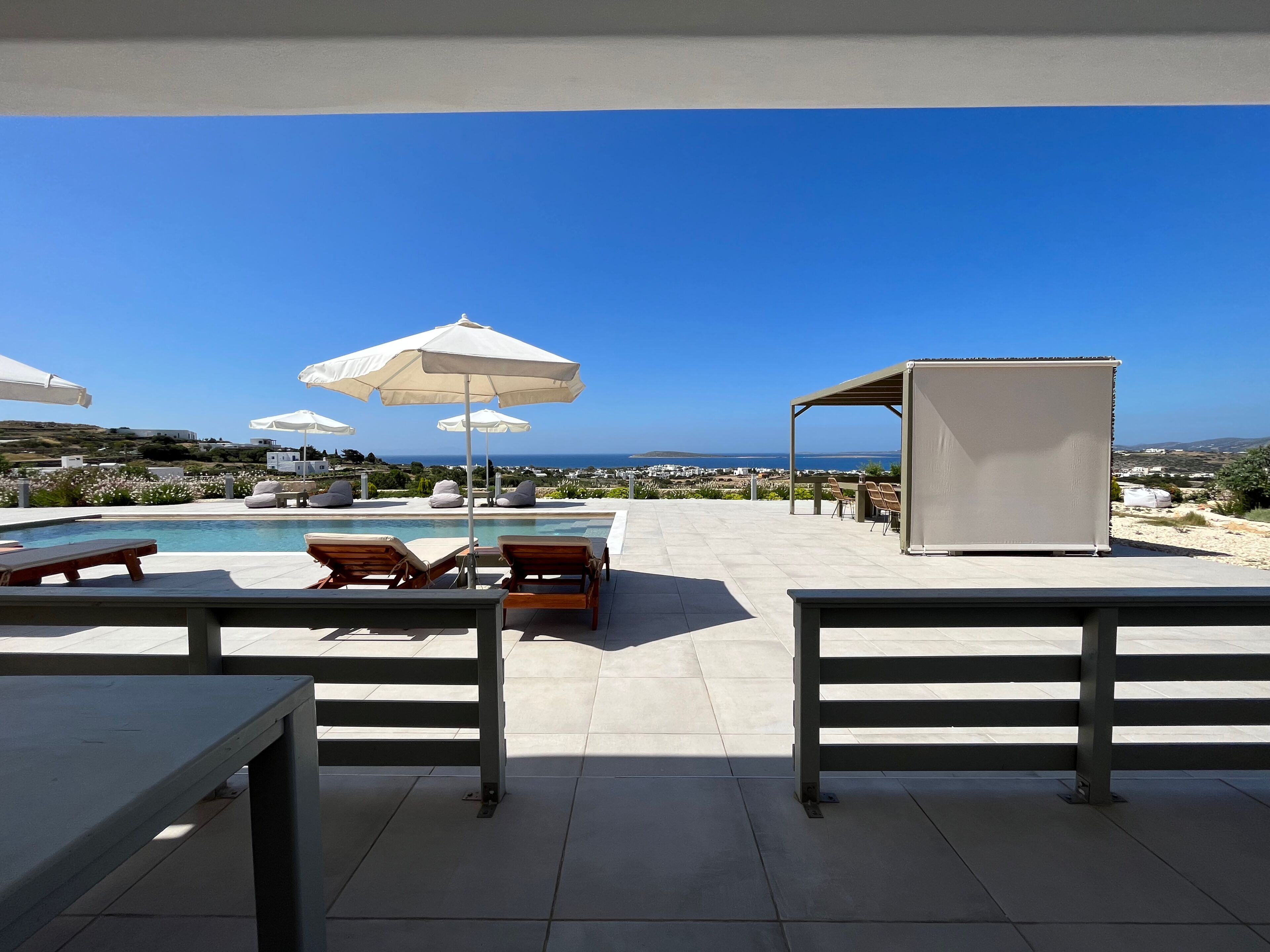 A poolside area with lounge chairs, umbrellas, and a view of the sea.