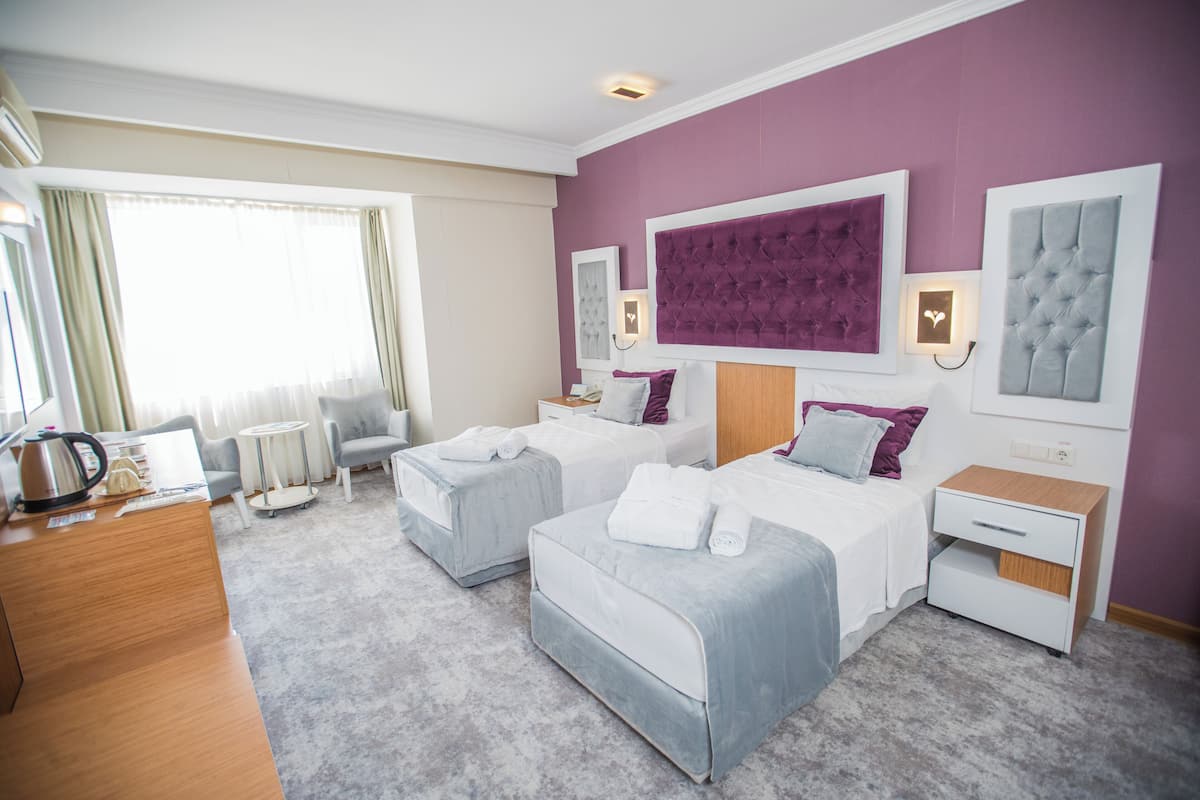 Una habitación de hotel con dos camas, un escritorio, una silla y un gran ventanal con cortinas.