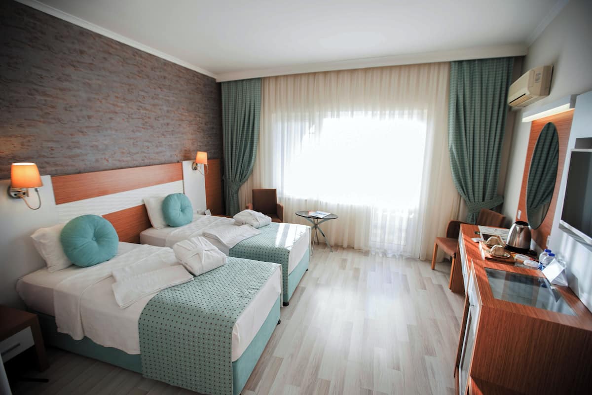 Una habitación de hotel con dos camas, una mesita, una silla, un escritorio y un televisor.